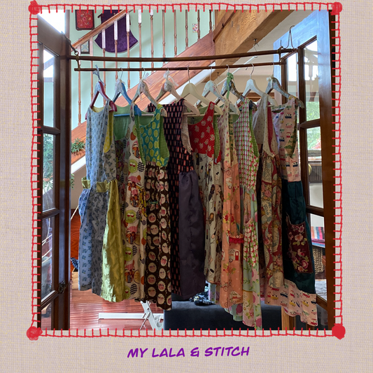 A row of handmade dresses hanging neatly on a simple rack, each with unique stitching, soft colors, and a cozy LALATOWN aesthetic, displayed as part of the Lala Closet collection.